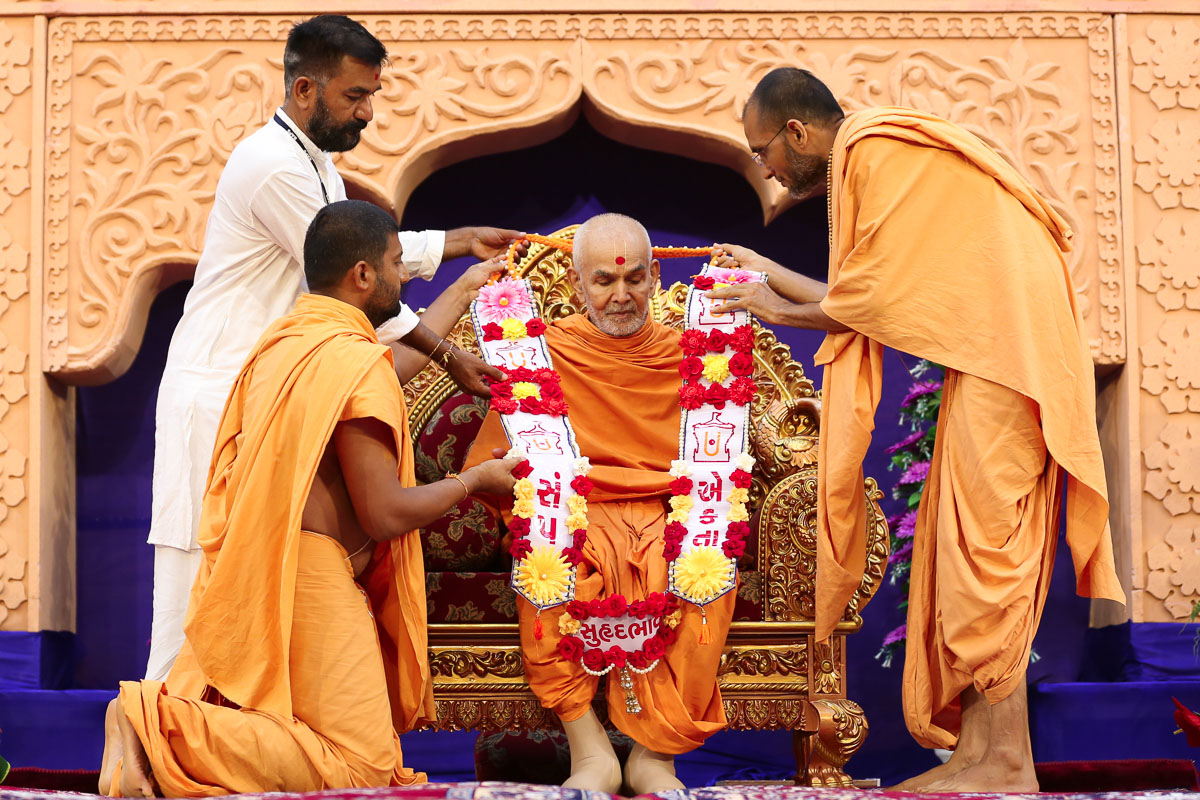 Sadhus and a devotee honor Swamishri with a garland