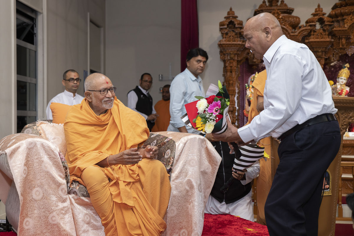 A devotee welcomes Pujya Kothari Swami with a bouquet of flowers