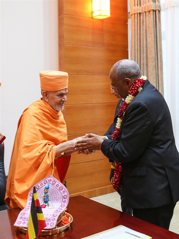 Swamishri honors Rt. Hon. Ruhakana Rugunda with a garland