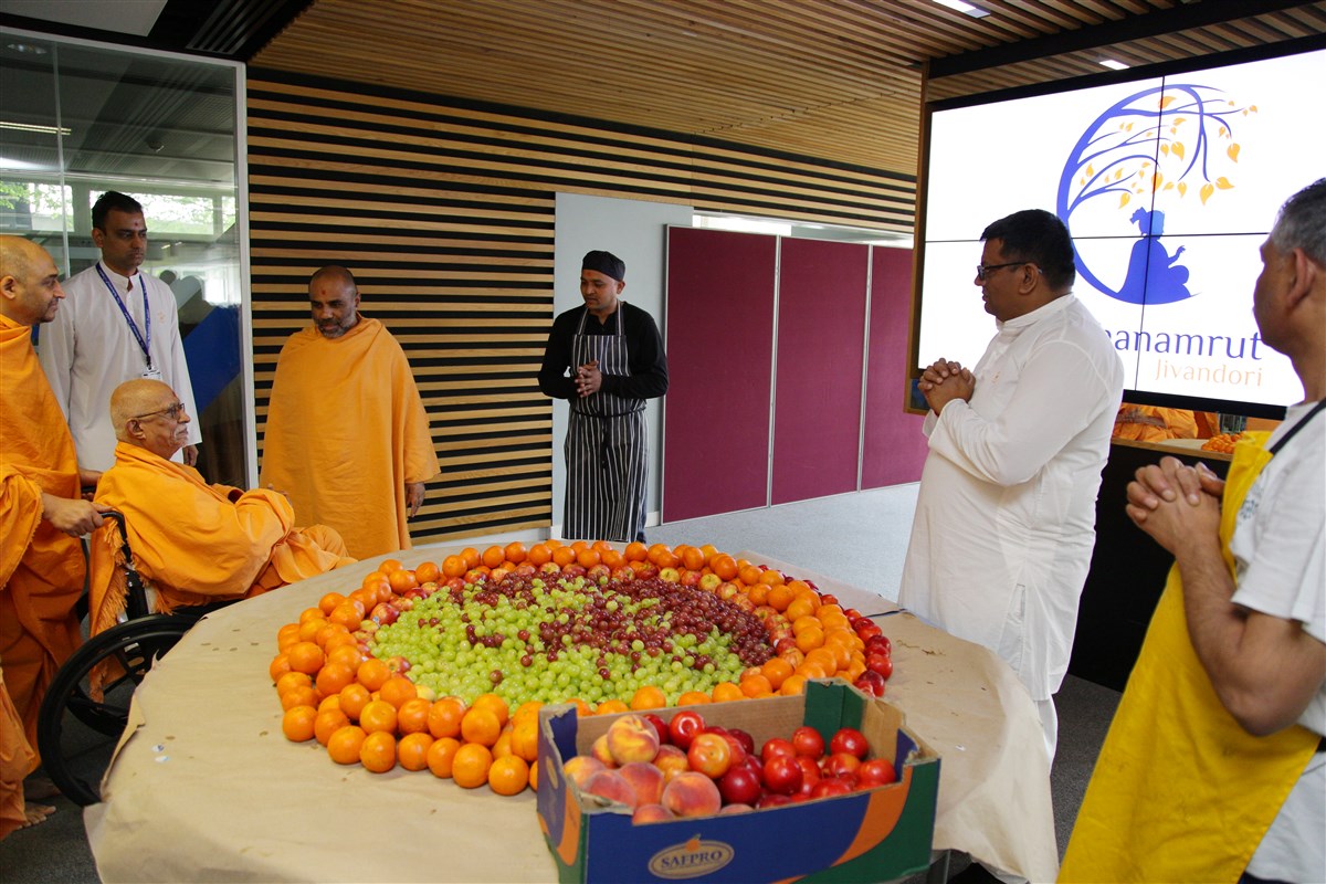Pujya Doctor Swami observes volunteers arranging a fruit table in preparation for lunch