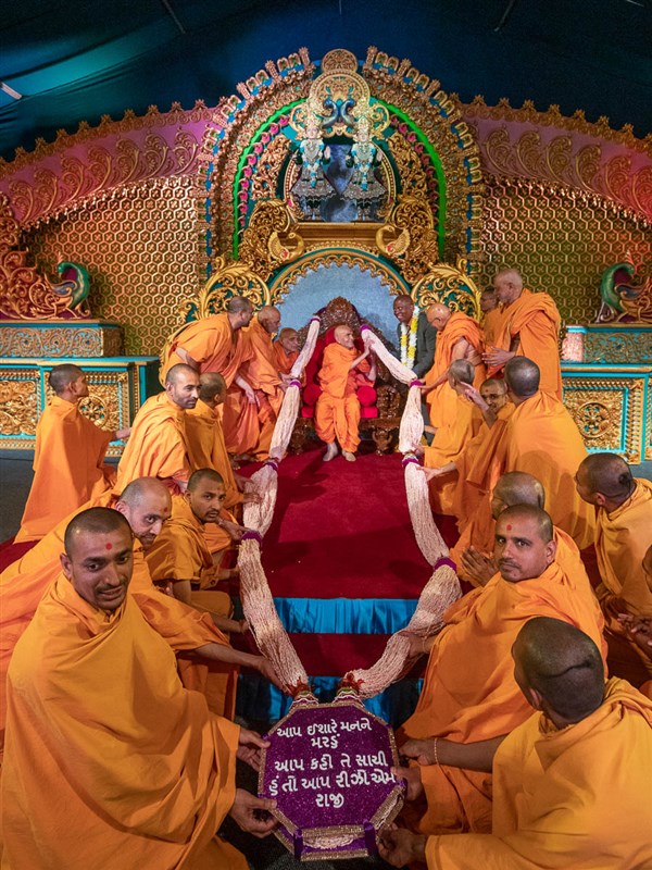 Sadhus honor Swamishri with a large garland of mamra (puffed rice)