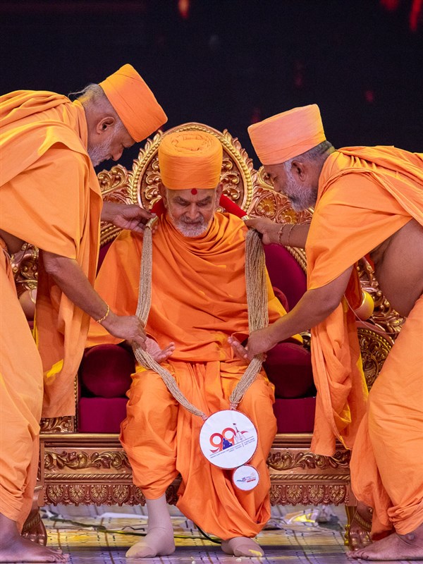 Rajeshwar Swami and Bhagyasetu Swami honor Swamishri with a garland
