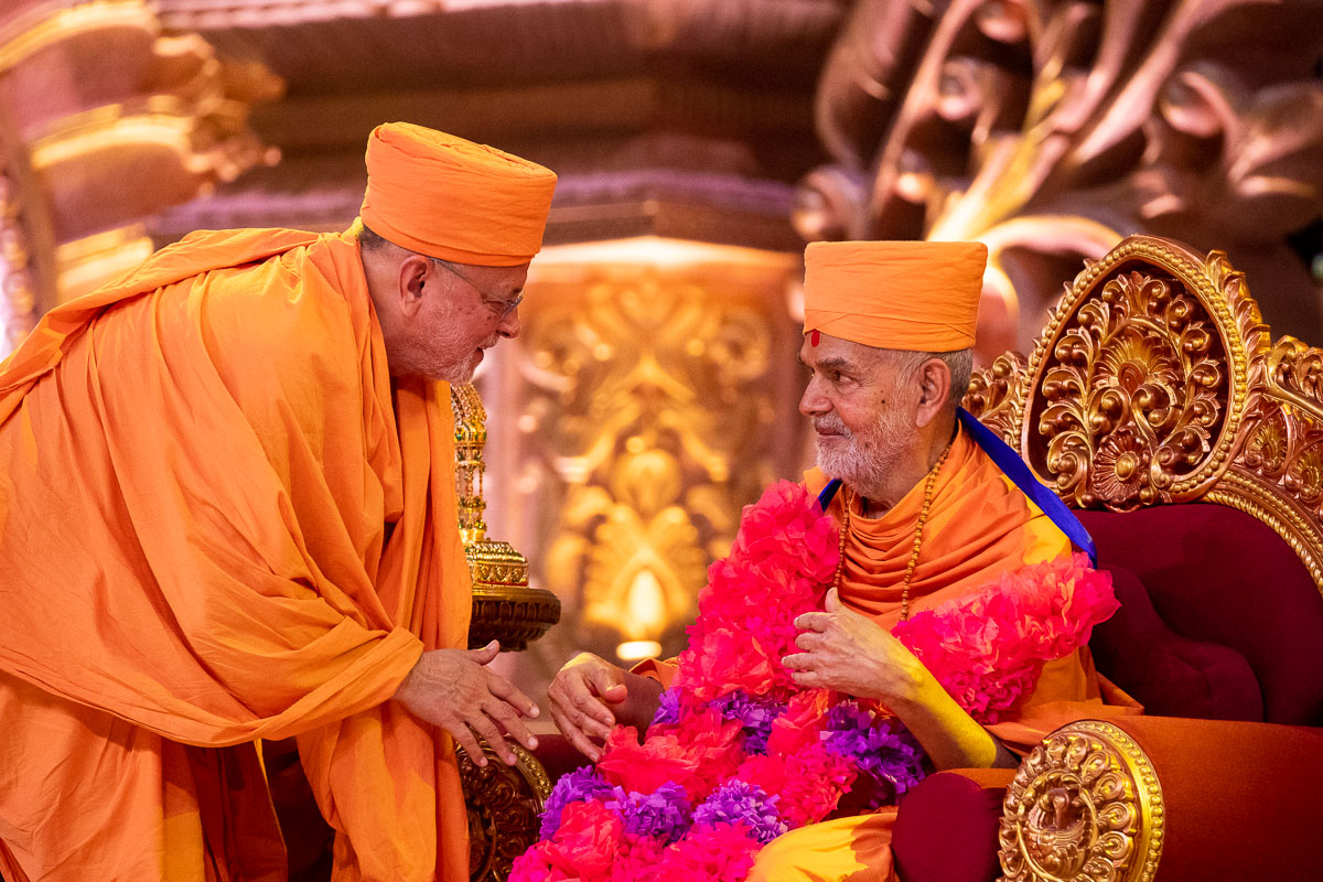 Pujya Ishwarcharan Swami honors Swamishri with a garland