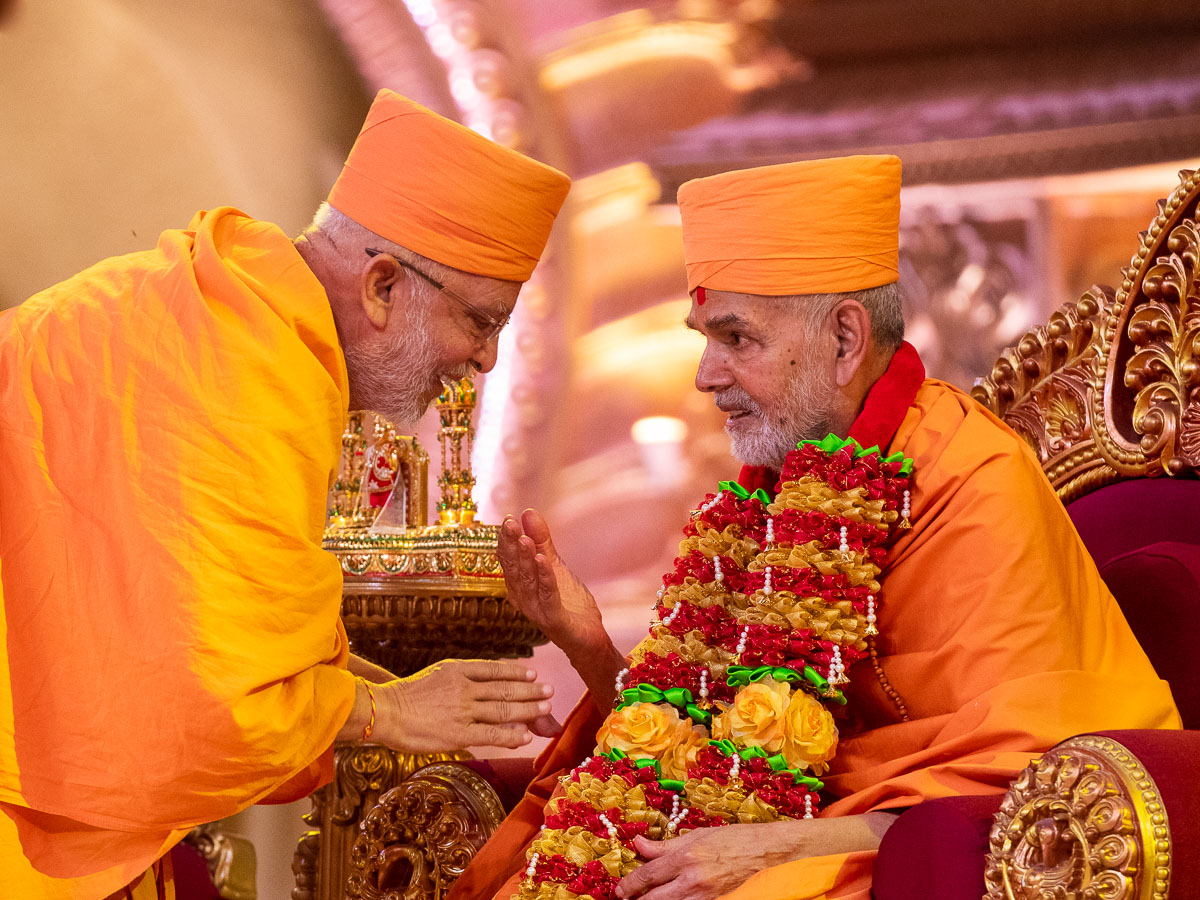 Pujya Ghanshyamcharan Swami honors Swamishri with a garland