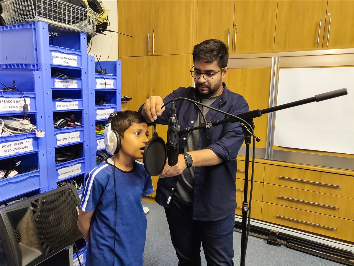 An audio volunteer facilitates the recording of individual vocals to be inserted in the musical elements within the production