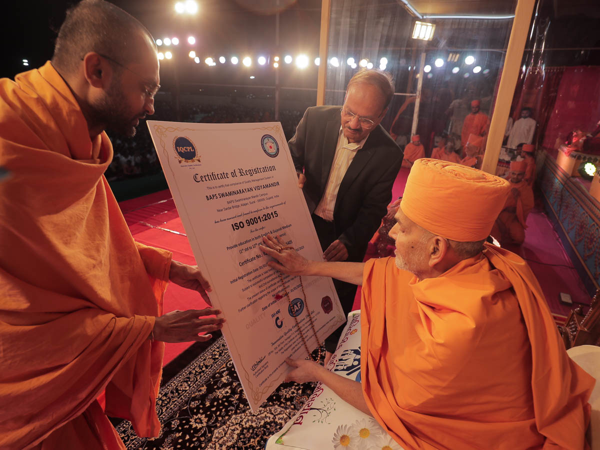 Swamishri sanctifies a certificate awarded to Swaminarayan Vidyamandir, Surat