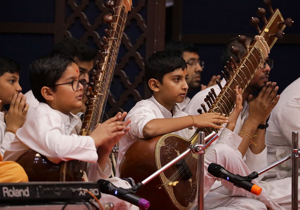 Children play the sitar while Swamishri greets all with folded hands