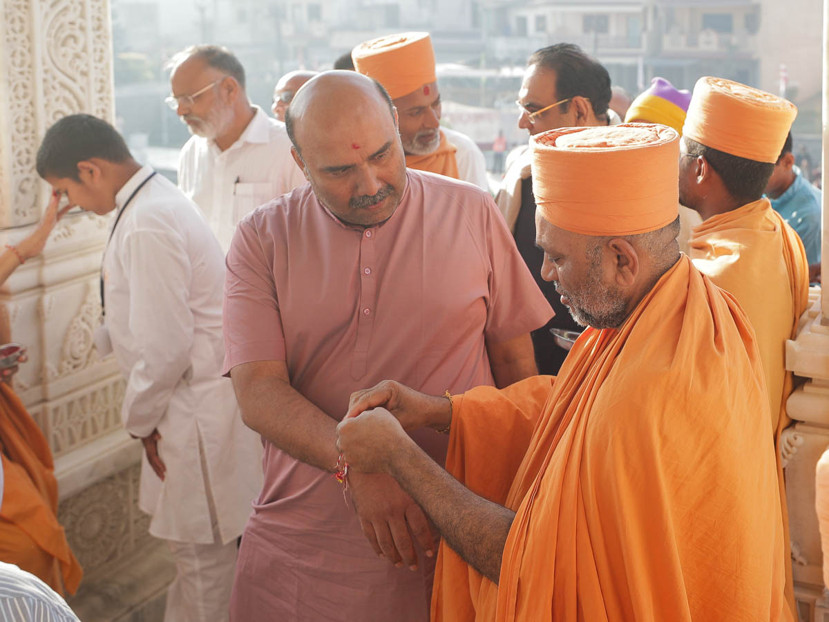 Sadhus tie a nadachhadi on devotees as they enter for the pratishtha mahapuja