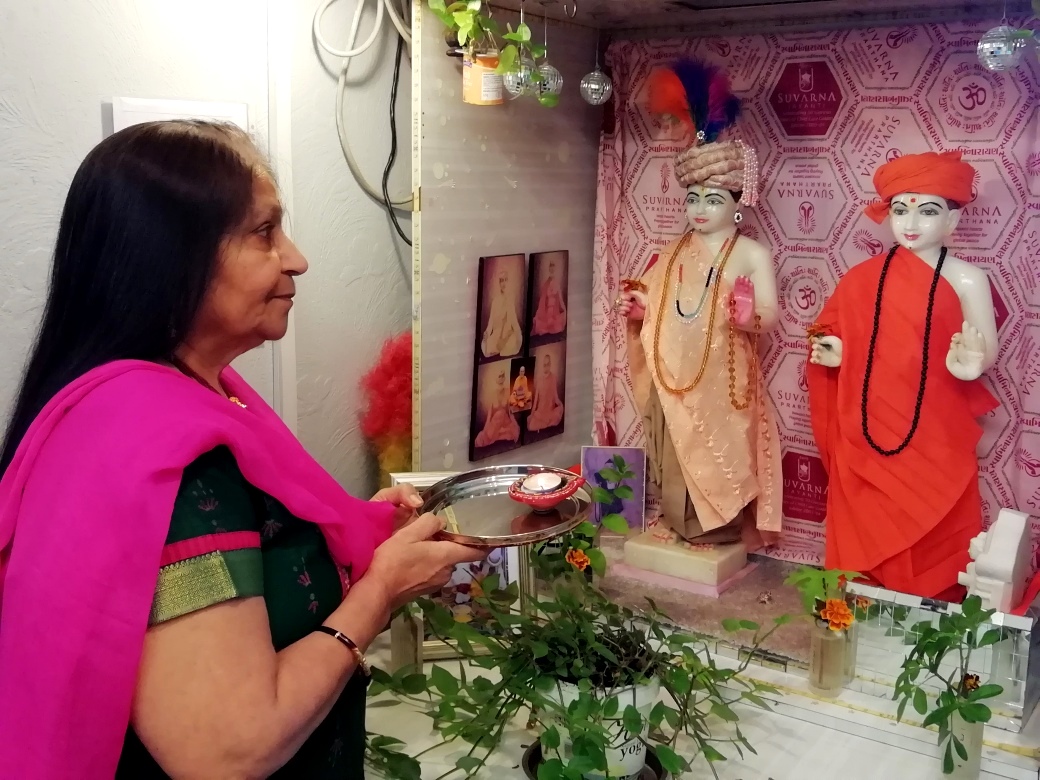 A mahila devotee performs the arti at her ghar mandir while participating in the virtual celebrations