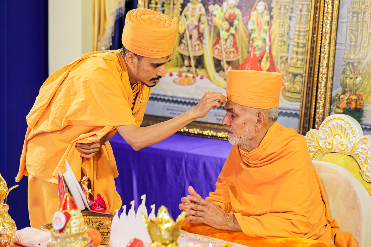 Santcharitdas Swami applied a tilak and rice grains on Swamishri's forehead, symbolising commitment for the mahapuja rituals