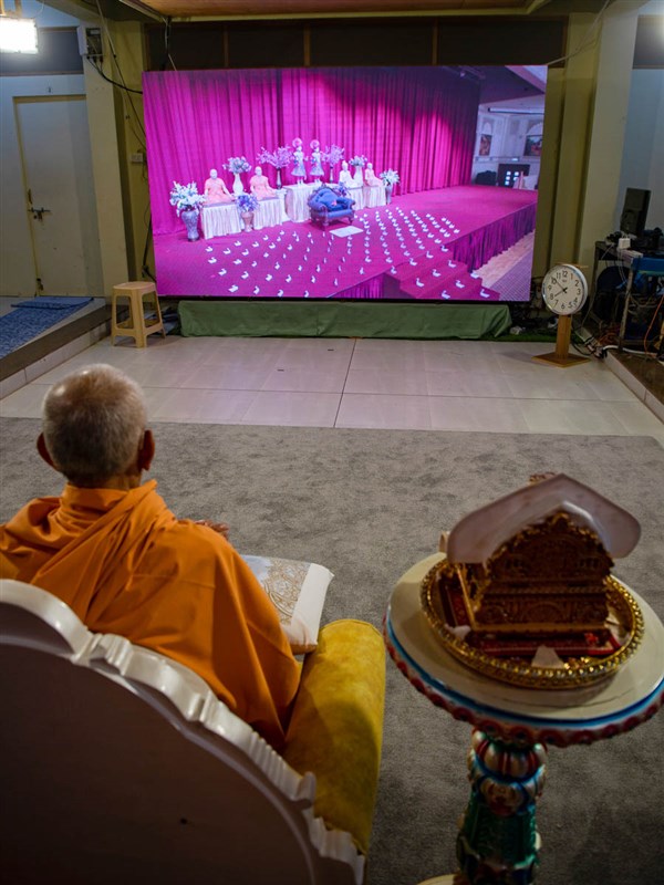 Swamishri watches the programme as his own swan is sat on his sinhasan in London amid thousands of others