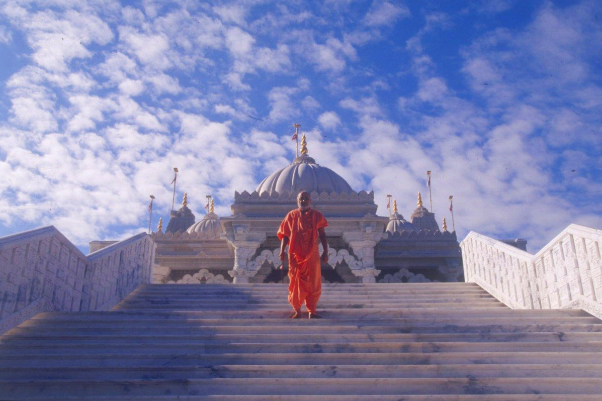 Pramukh Swami Maharaj stands on the steps of the mandir; the first of its kind outside India and the template for future mandirs in the west