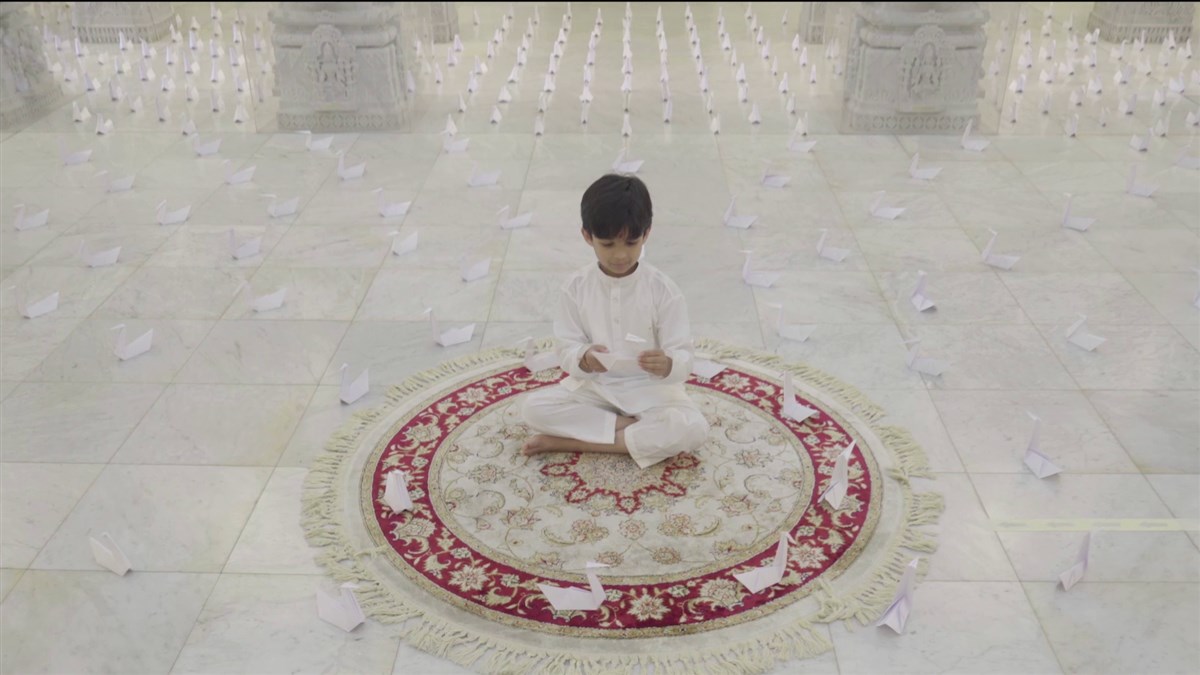 As the child completes his final fold, hundreds of swans are revealed surrounding him under the central dome of the mandir
