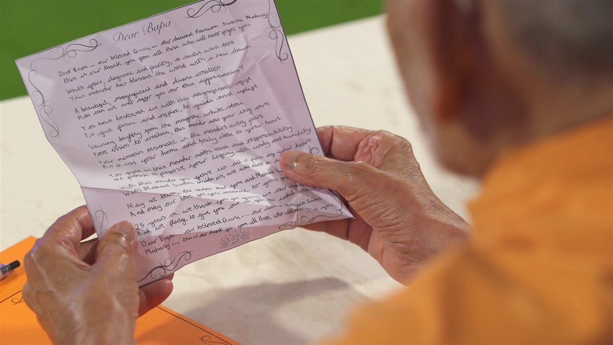 Mahant Swami Maharaj unfolds the swan and reads the child’s letter thanking Pramukh Swami Maharaj for gifting us London Mandir