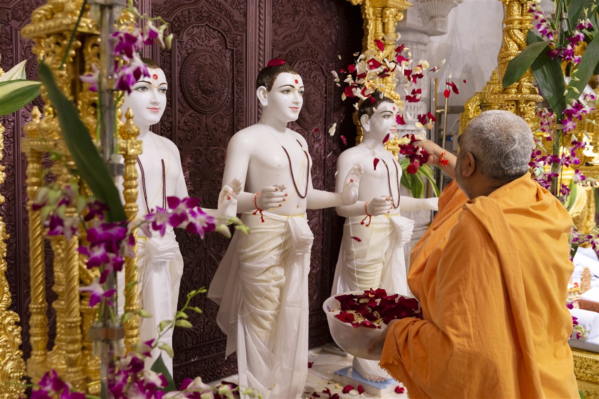 Yogvivekdas Swami offers an abhishek of flower petals to Aksharbrahma Gunatitanand Swami, Parabrahma Purushottam Bhagwan Swaminarayan and Aksharmukta Gopalanand Swami
