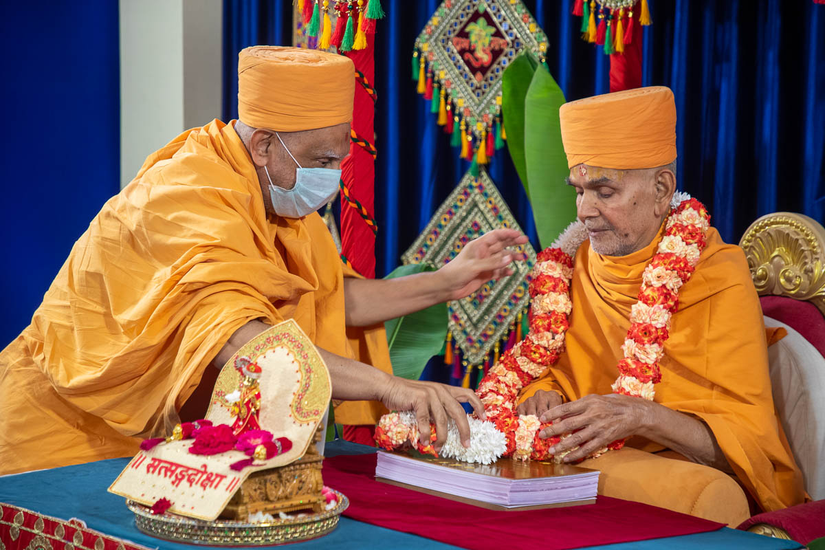 Atmaswarup Swami honors Swamishri with the sanctified garland