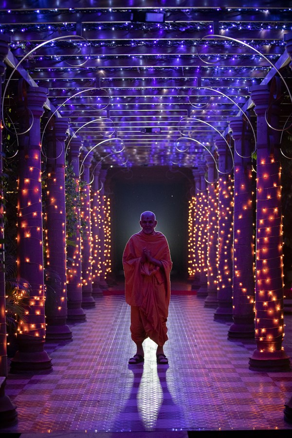 Swamishri stands amid a colonnade decorated with festive lights