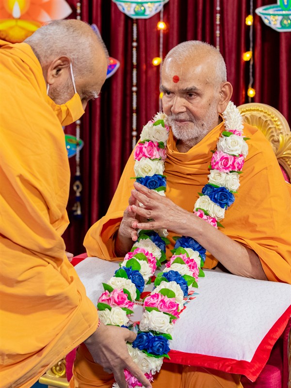 Pujya Atmaswarup Swami honors Swamishri with a garland