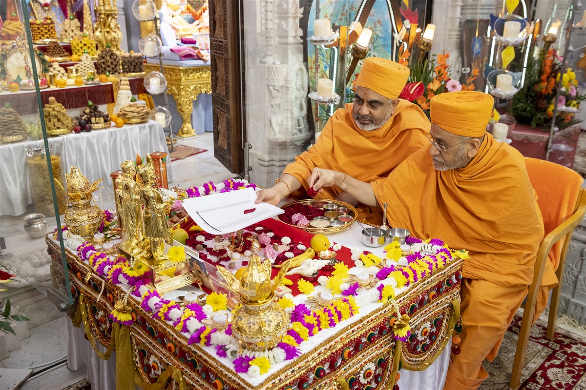 Swamis offer a list of supporters' names to the murtis, seeking blessings on their behalf