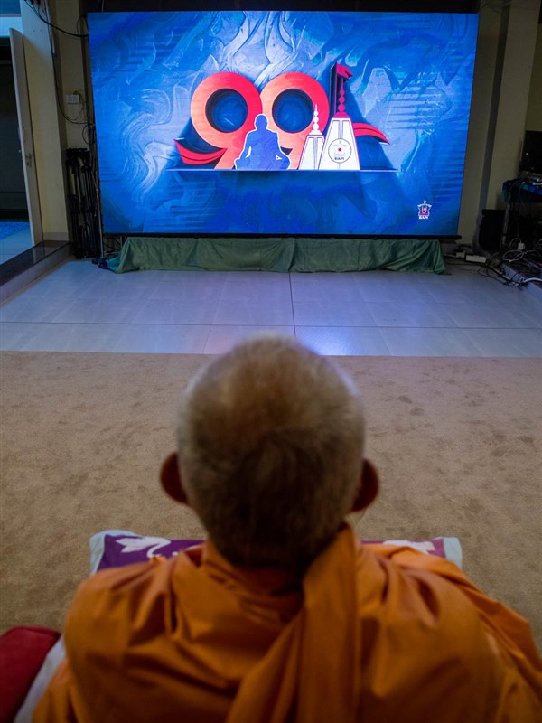 Swamishri watches the Pramukh Swami Maharaj 99th Janma Jayanti celebration assembly