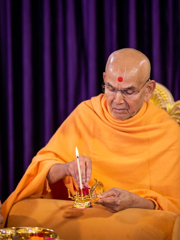 Swamishri performs pujan of arti with a flower