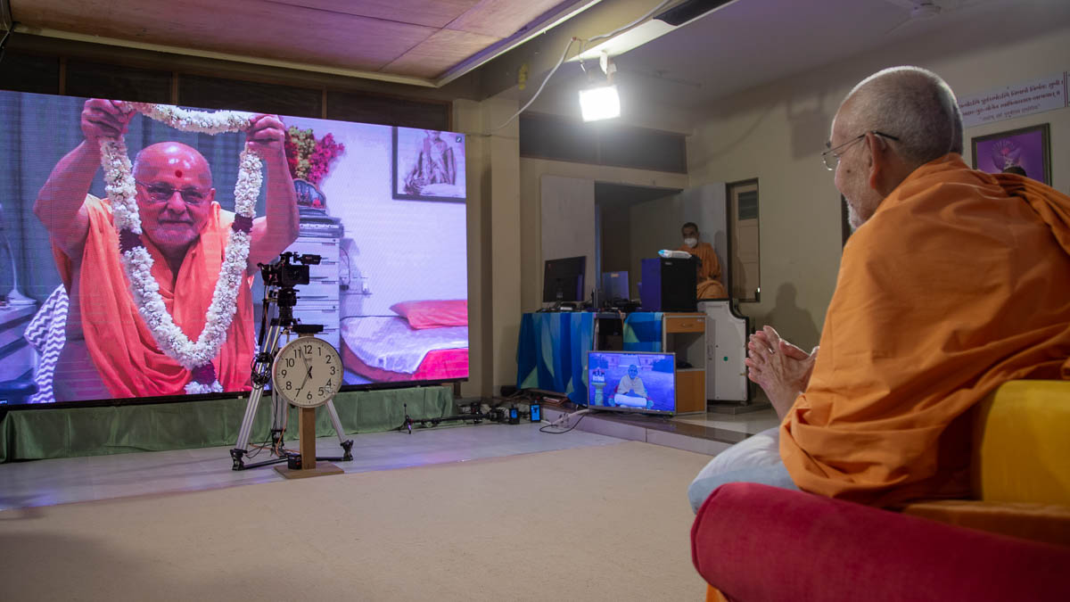 Pujya Ishwarcharan Swami honors Swamishri with a garland via video conference