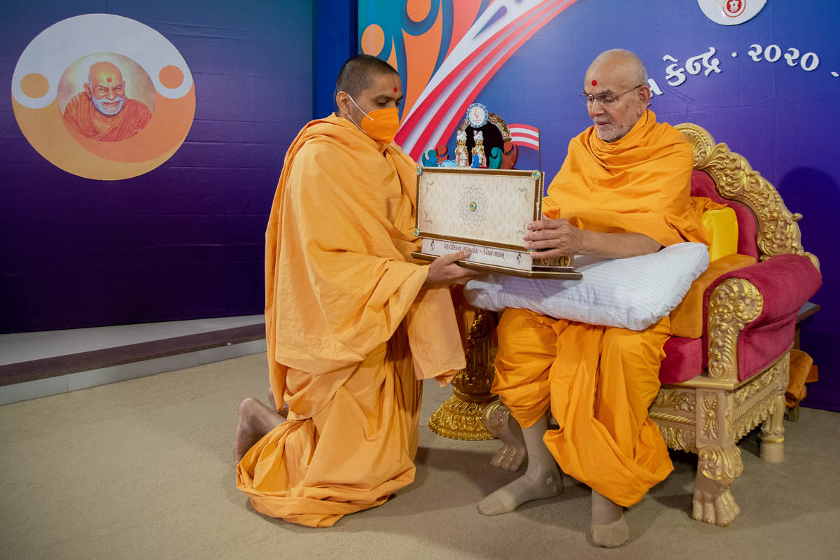 Swamishri sanctifies an invitation card for the evening Yuva Talim Kendra convocation assembly
