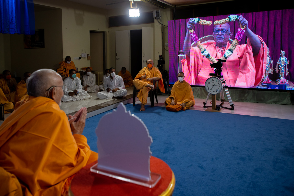 Pujya Doctor Swami honors Swamishri with a garland via video conference from Sarangpur
