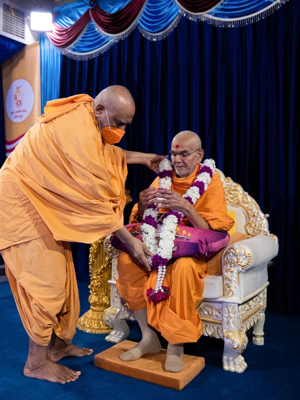Atmaswarup Swami honors Swamishri with a garland