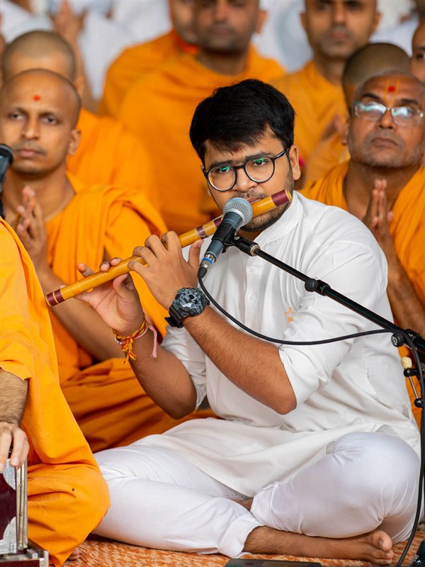 A youth plays a flute in Swamishri's daily puja