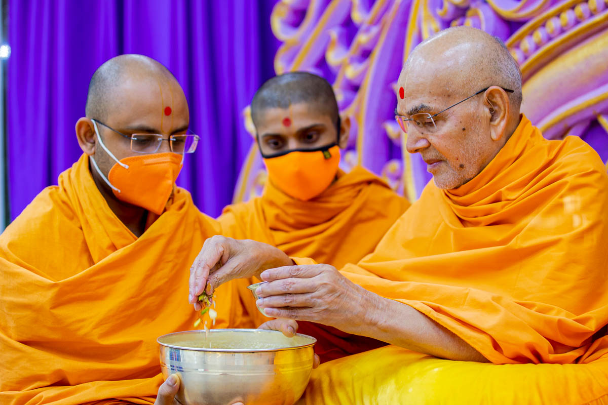 Swamishri adds dry fruits to dudhpak to be served after the Shastriji Maharaj Smruti Sabha