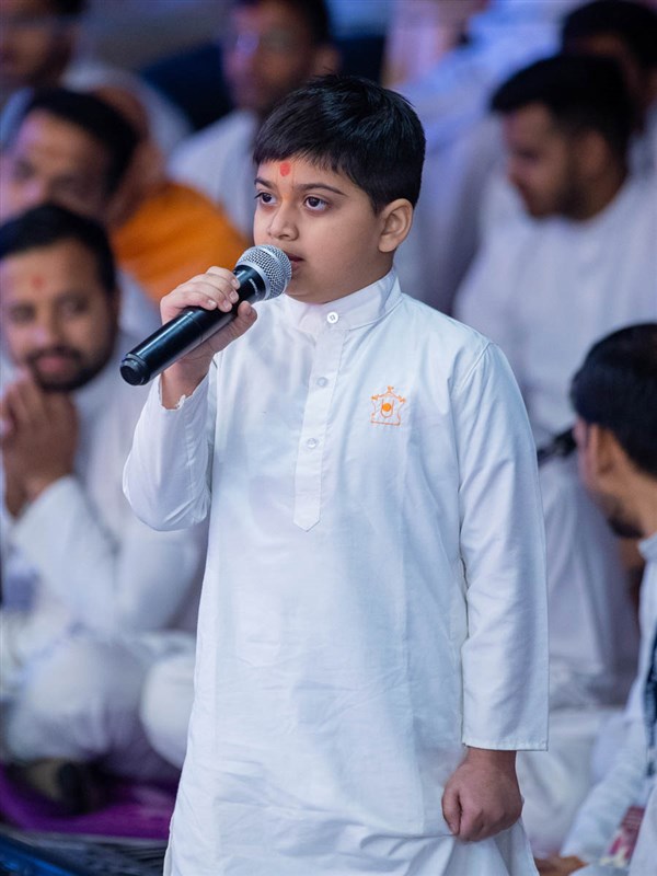 A child leads everyone in reciting the sadhana mantra and daily prayer in Swamishri's puja