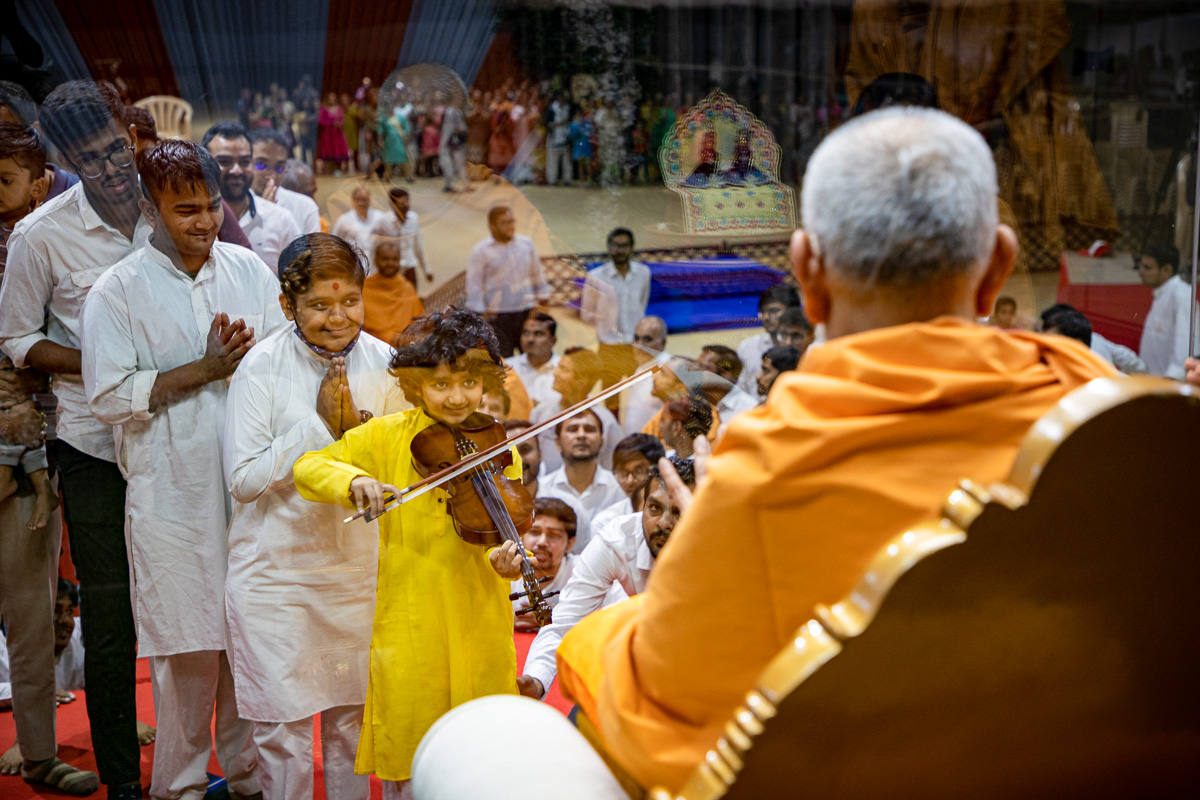 A child plays the violin before Swamishri