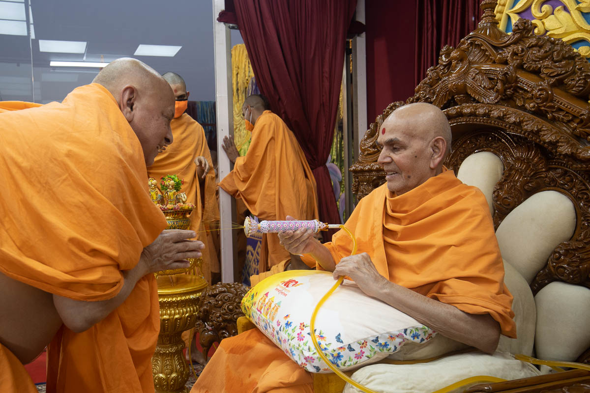 Swamishri sprays sanctified saffron-scented water on Pujya Ishwarcharan Swami