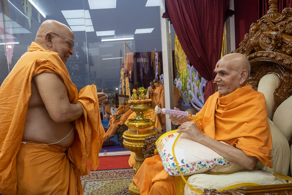 Swamishri sprays sanctified saffron-scented water on Pujya Ghanshyamcharan Swami