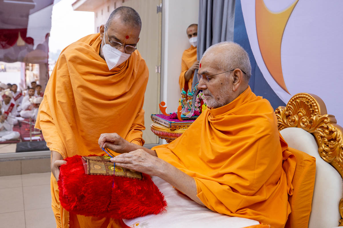 Swamishri sanctifies an invitation card for the evening Yuva Talim Kendra assembly
