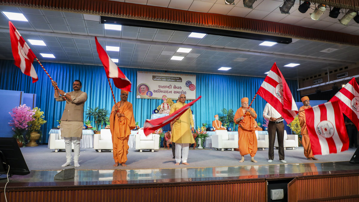 Pujya Ishwarcharan Swami, Shri Bhupendrabhai Patel, Shri Jitubhai Vaghani, Shri Jagdishbhai Panchal and sadhus wave BAPS flags
