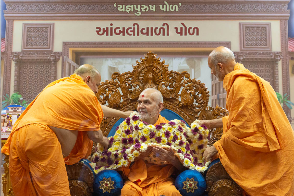 Pujya Ishwarcharan Swami and Pujya Viveksagar Swami honor Swamishri with a flower shawl