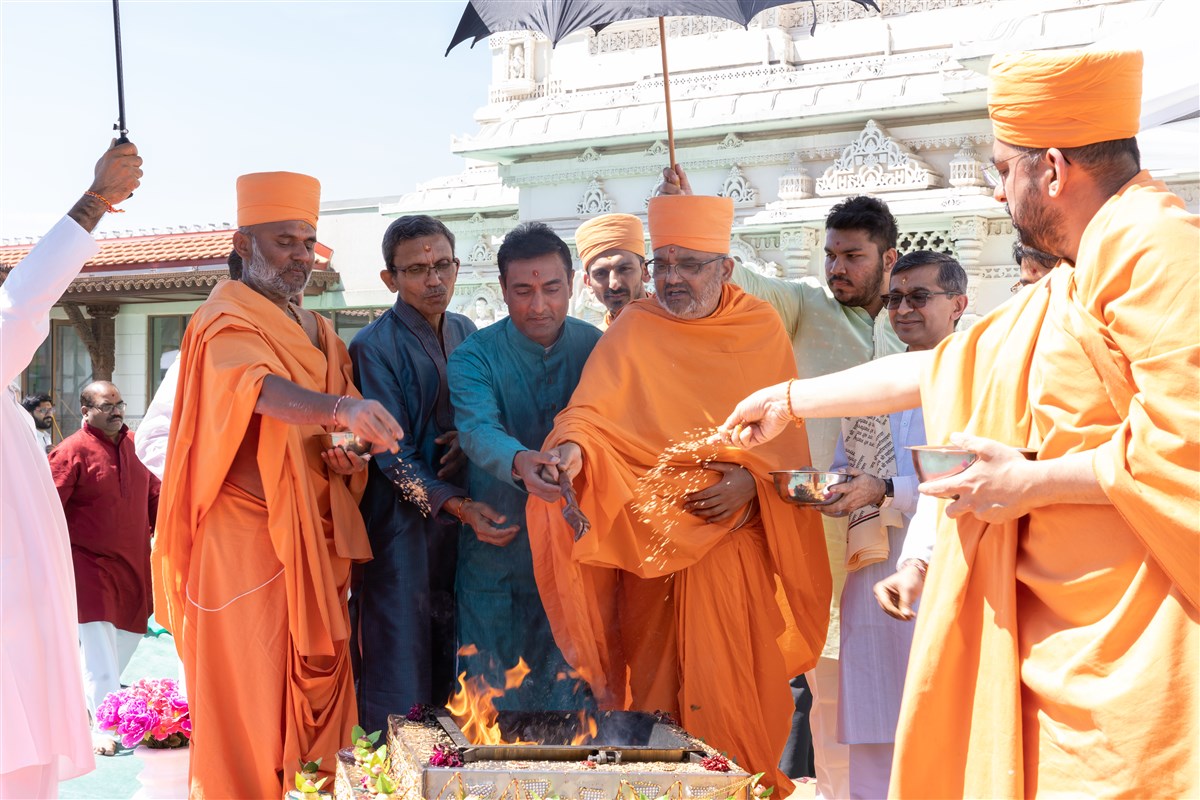 Pujya Swamis and devotees offer sanctified grains in the sacrificial flame