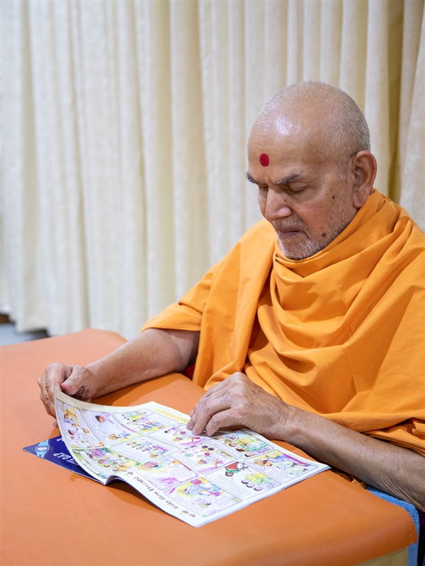 Swamishri reads the latest English issue of 'Swaminarayan Bal Prakash'