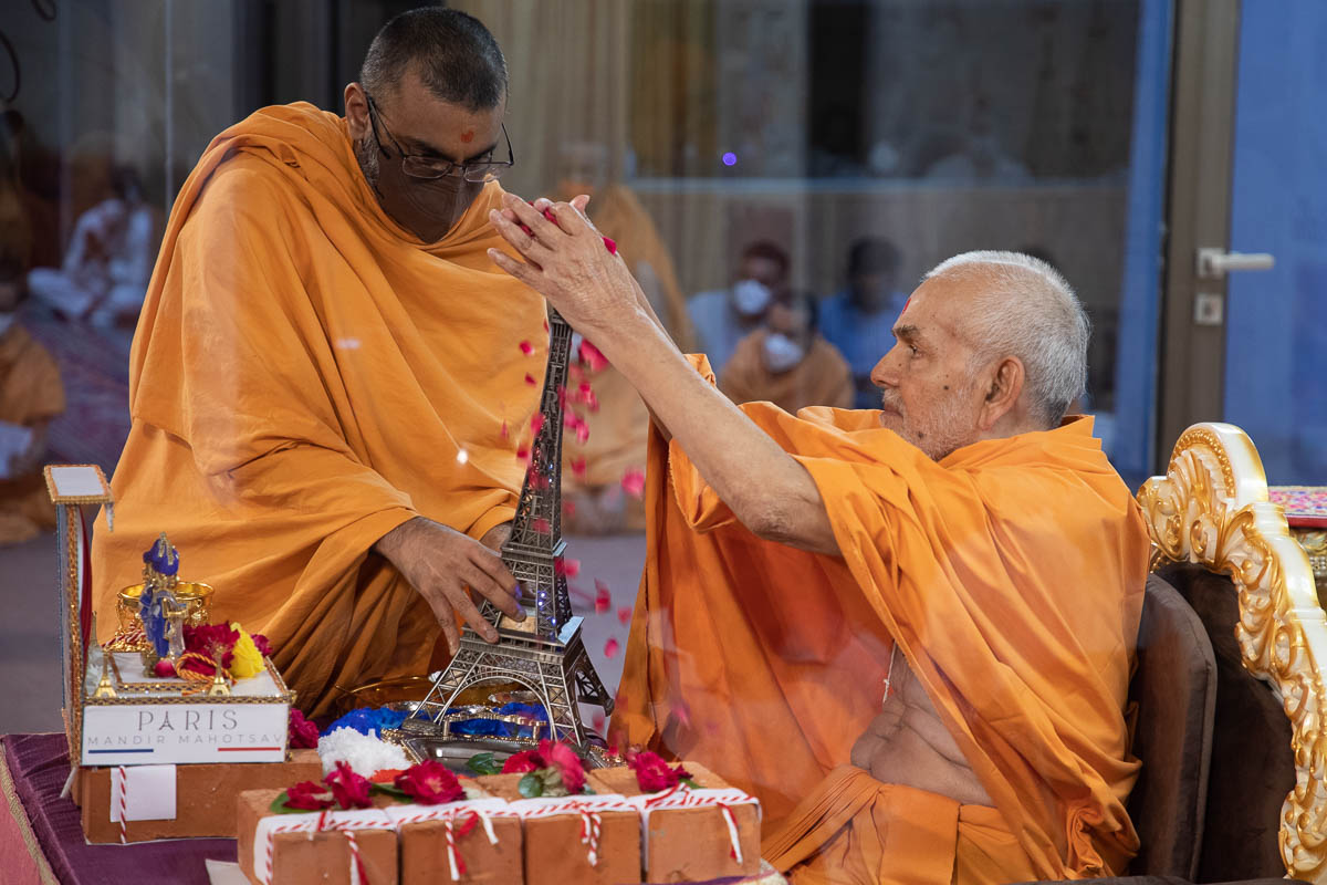 Swamishri showers flower petals on a model of the Eiffel Tower
