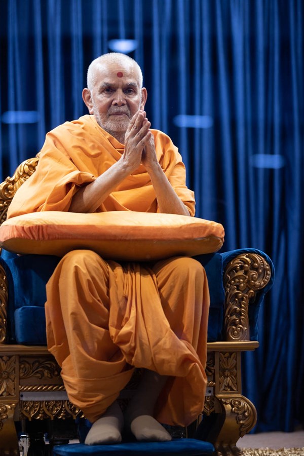 Swamishri greets all with folded hands in the Pramukh Swami Auditorium