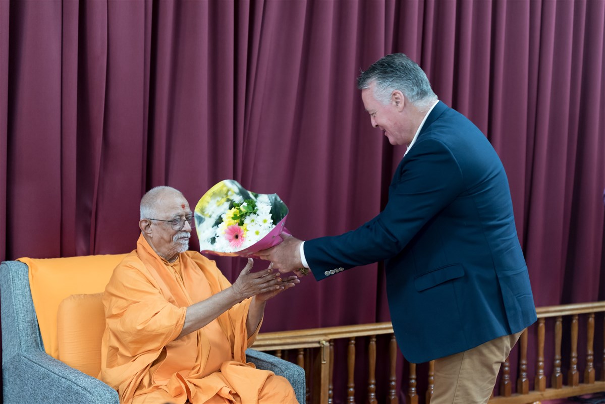 Mr Michael Healy offers a flower bouquet to Pujya Doctor Swami