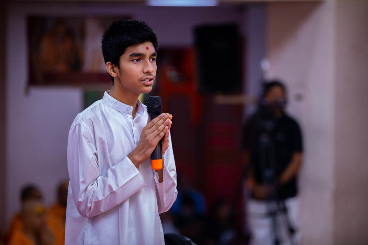 A youth leads everyone in reciting the sadhana mantra and daily prayer in Swamishri's puja