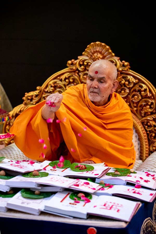 Swamishri showers sanctified rice grains and flower petals onto the accounts books