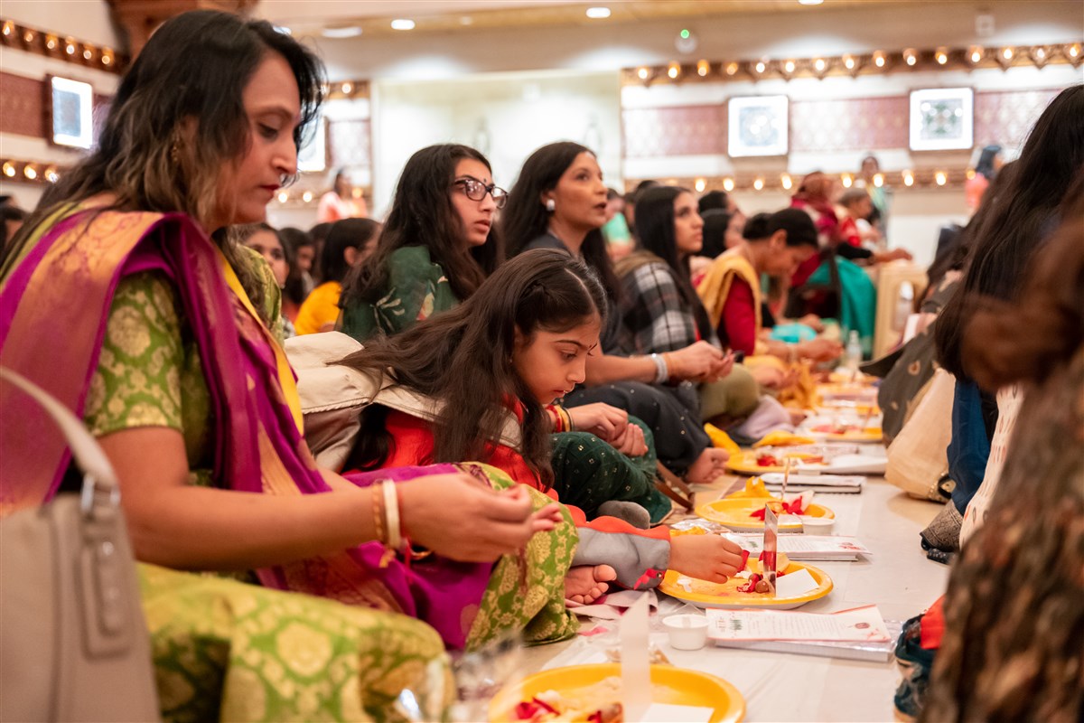 A young girl participates in the Chopda Pujan with her sister and mother at her side.