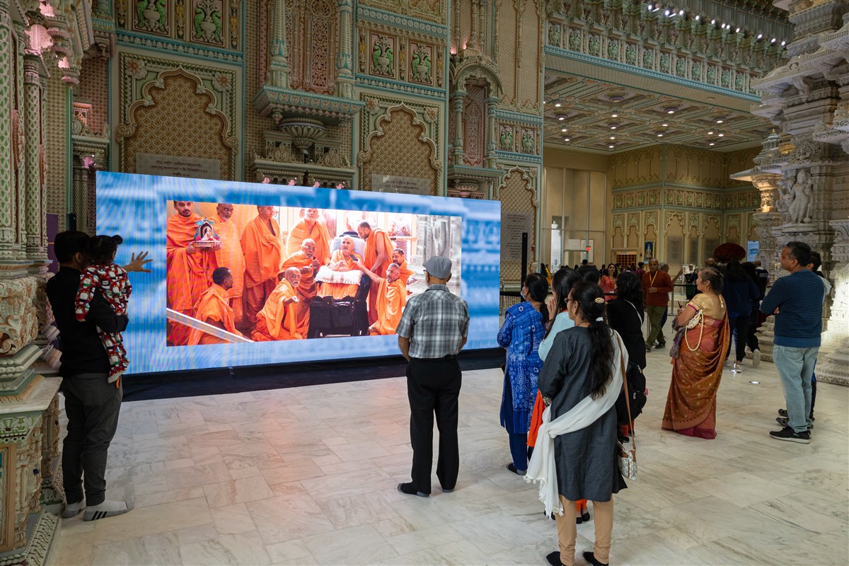  Visitors closely watch a video of Swamiji's visit in 2014.