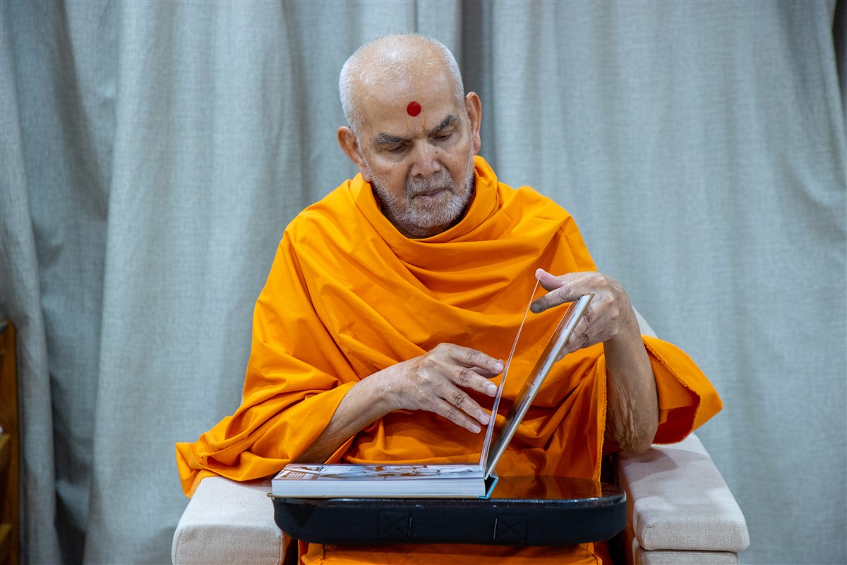 Swamishri looks through a photobook of Brahmaswarup Pramukh Swami Maharaj