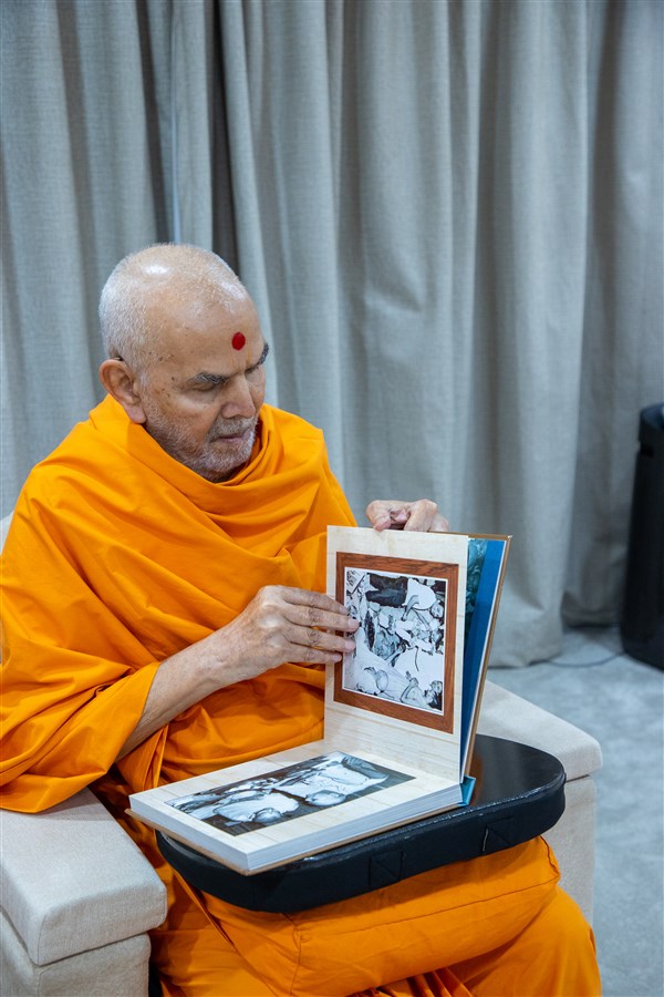 Swamishri looks through a photobook of Brahmaswarup Pramukh Swami Maharaj