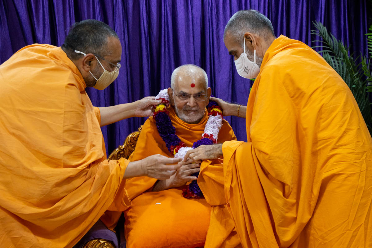 Anandswarup Swami and Vishwavihari Swami honor Swamishri with a garland
